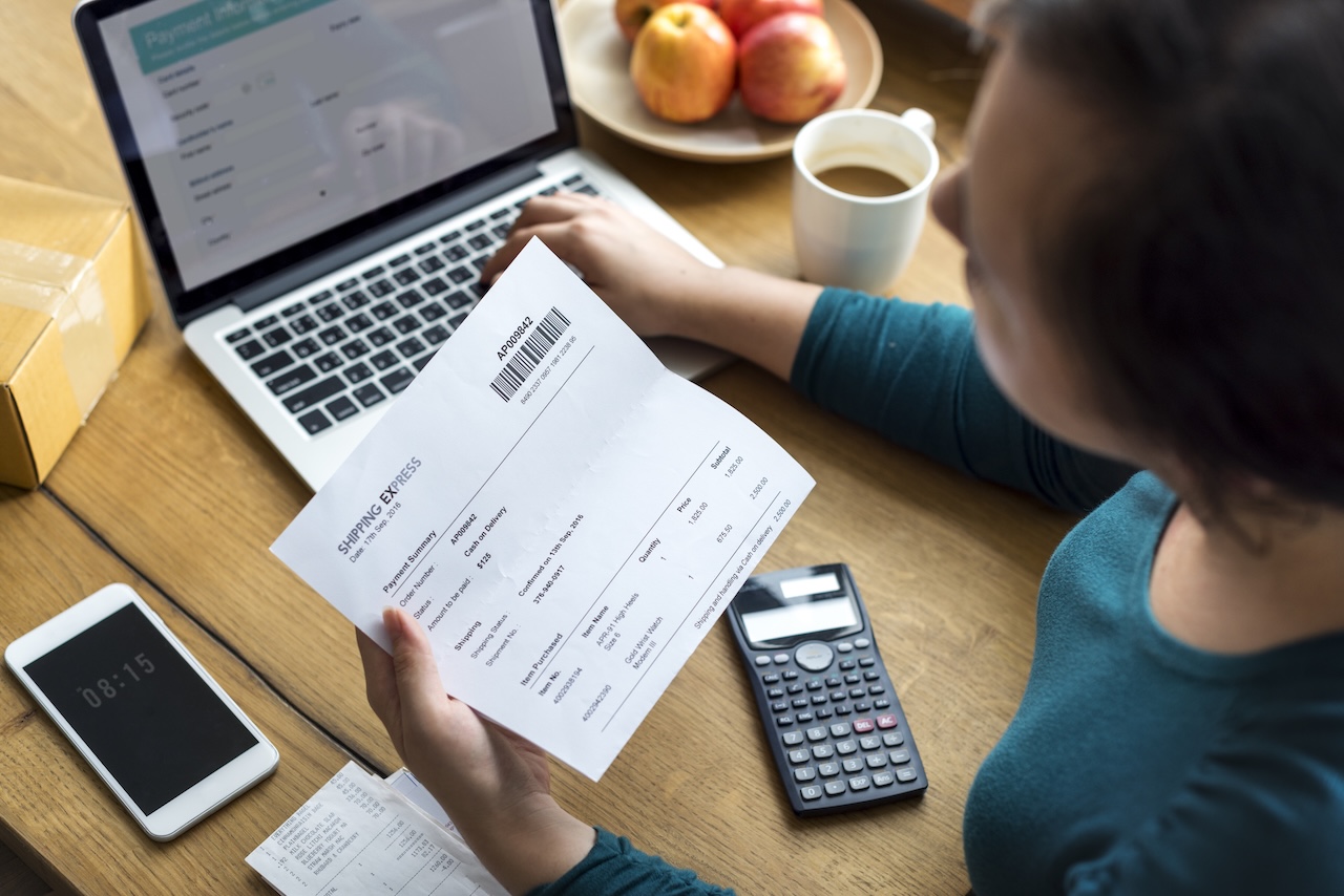 Small business owner checking paper invoices against a laptop